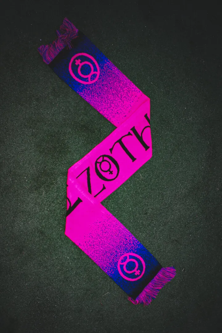 A knitted pink and blue AZOTH scarf, laid out in a zigzag