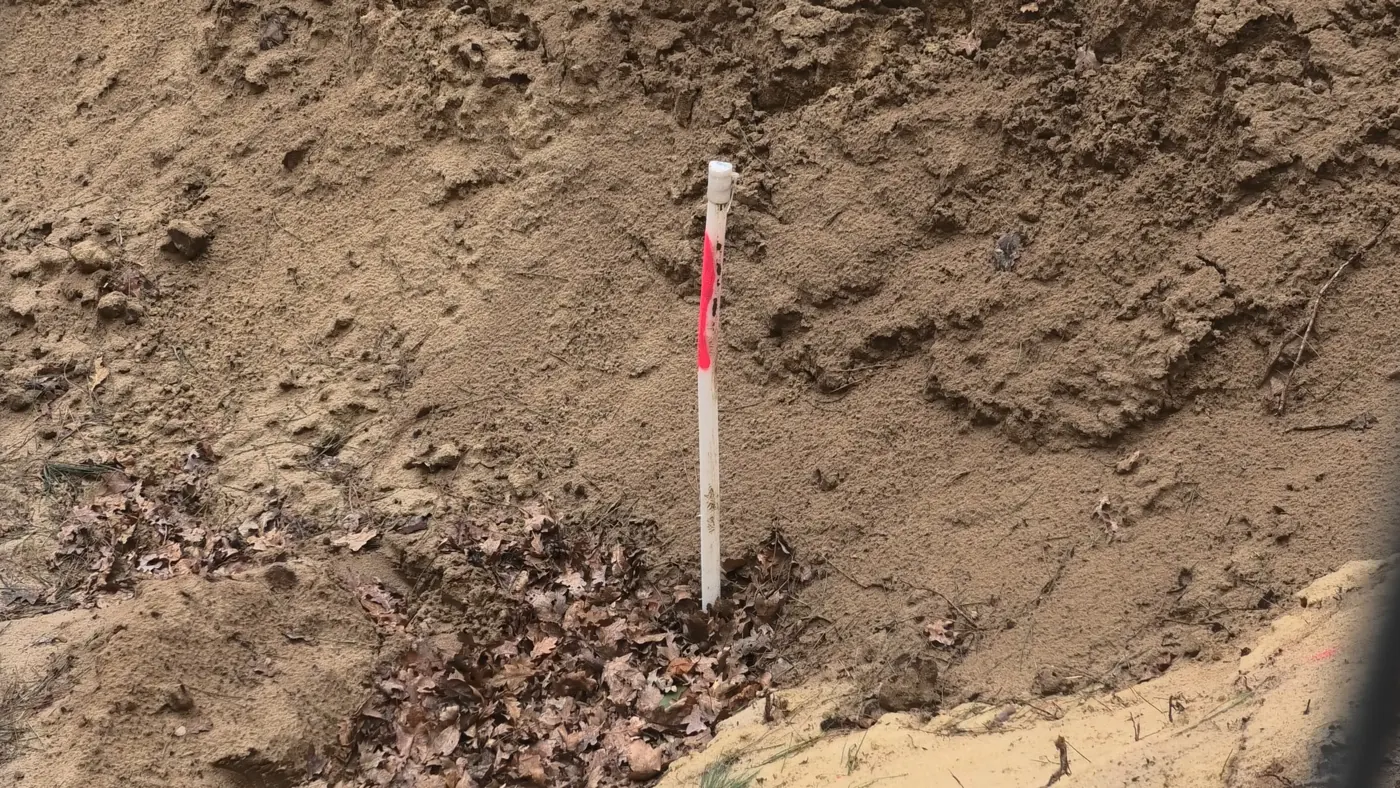 A measuring rod in the sandy soil of the dump site
